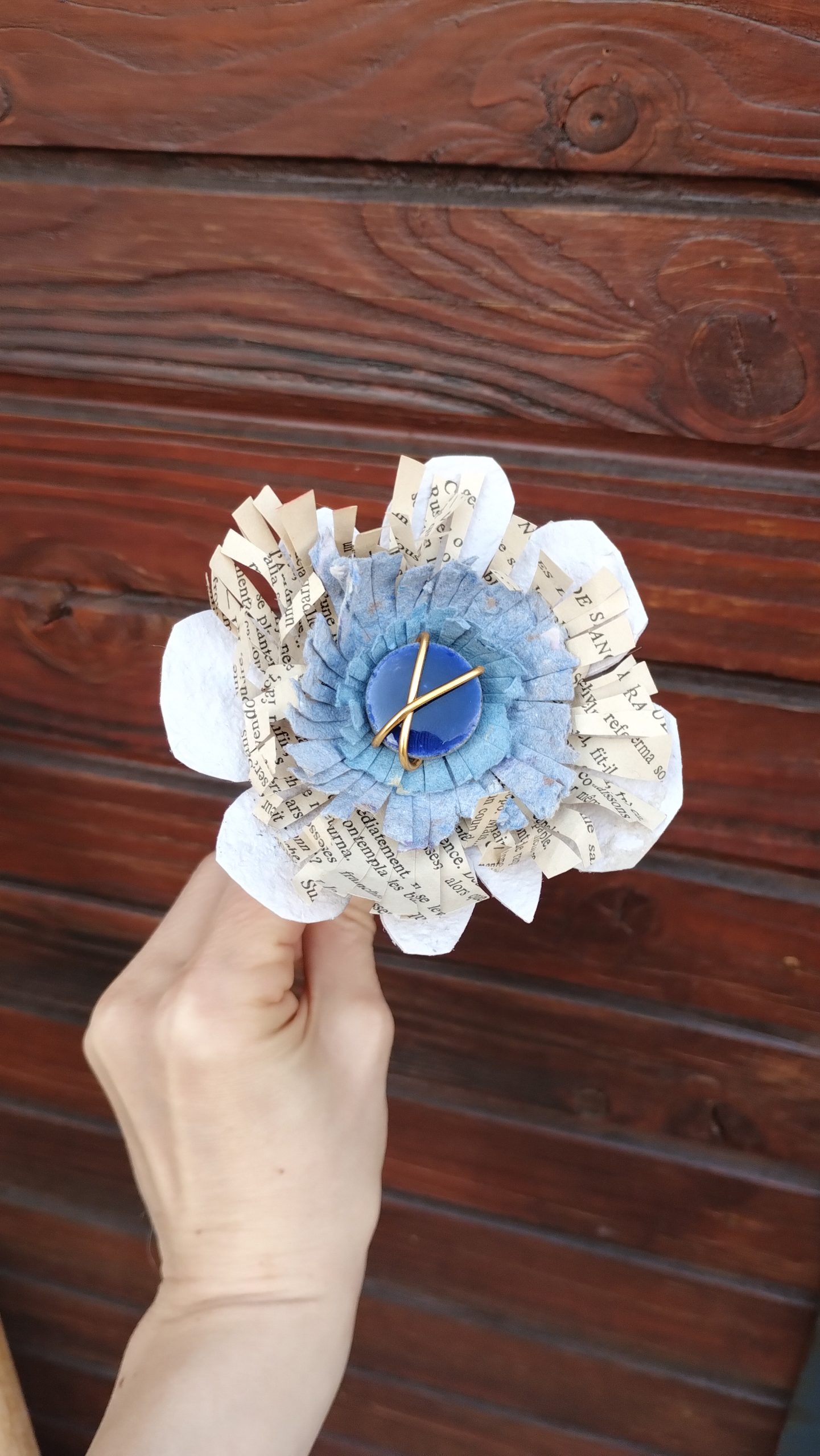 fleur en papier recyclé et feuille de livre avec une lave émaillée en son centre.